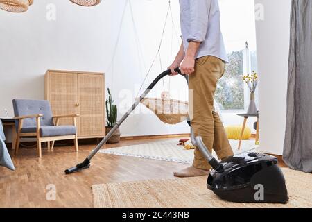 Baby Junge auf Schaukel Blick auf Vater Reinigung Wohnzimmer mit Staubsauger Stockfoto