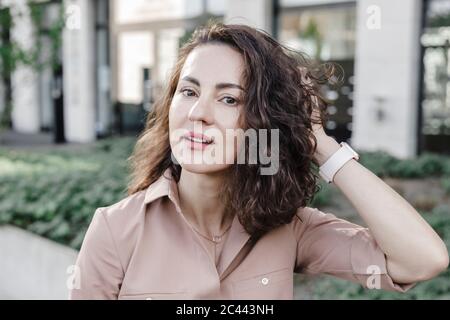 Selbstbewusste Geschäftsfrau mit Hand in Haar außerhalb des Bürogebäudes Stockfoto