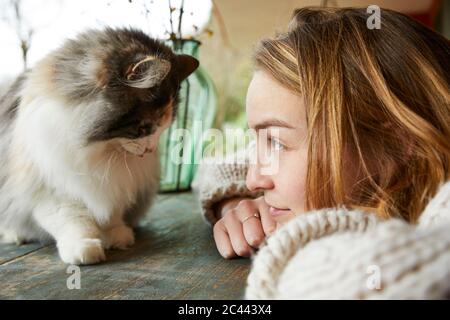Junge Frau, die im Freien auf einem Holztisch eine norwegische Waldkatze anschaut Stockfoto