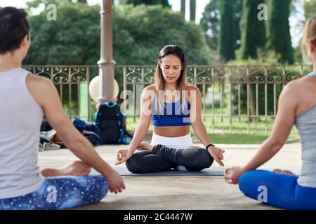 Yoga-Lehrer üben Lotusstellung mit Mann und Frau im Pavillon im Ciutadella Park Stockfoto