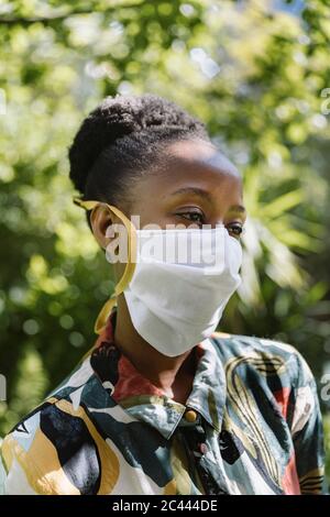 Portrait der jungen Frau trägt weiße Textil-Schutzmaske im Garten Stockfoto