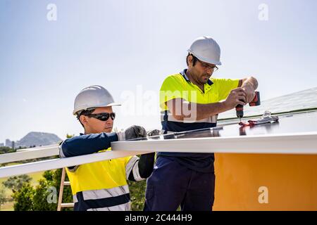Männliche Techniker installieren Sonnenkollektoren auf Hausdach gegen Himmel während sonnigen Tag Stockfoto