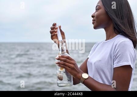 Profil der jungen Frau vor dem Meer, die in einer Flasche Nachricht sendet Stockfoto