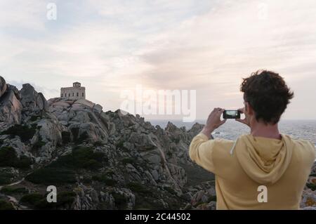 Rückansicht des Touristen fotografieren Leuchtturm, Capo Testa, Sardinien, Italien Stockfoto