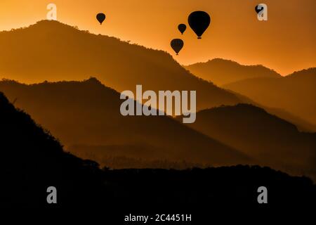 Indonesien, West Nusa Tenggara, Silhouetten von Heißluftballons, die in stimmungsvoller Dämmerung über Sumbawa fliegen Stockfoto