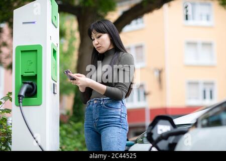 Carsharing, Frau, die ein Elektroauto mit dem Smartphone mietet Stockfoto