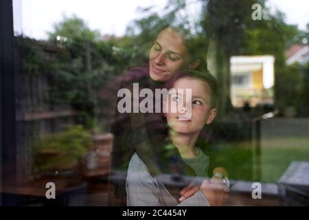 Frau mit geschlossenen Augen umarmenden Sohn zu Hause durch Fenster gesehen Stockfoto