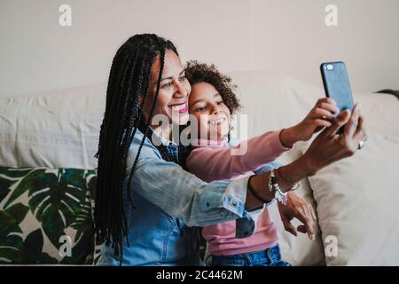 Glückliche Mutter und ihre kleine Tochter, die zu Hause Selfie mit dem Smartphone macht Stockfoto