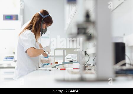 Weibliche Arzt trägt Gasmaske hält Glas während der Forschung im Labor Stockfoto