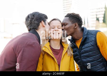 Zwei junge Männer küssen lächelnde junge Frau im Freien Stockfoto