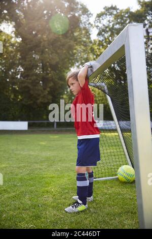 Junge in Fußballuniform hält Torpfosten auf dem Feld Stockfoto