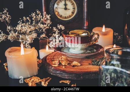 Eine Vintage rot weiß und Gold gefärbte Teetasse auf einer hölzernen Plattform auf einem schwarzen Tischaltar platziert. Küchenhexerei mit Tee, Kräutern und Gewürzen Stockfoto