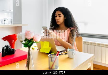 Junge Frau, die von zu Hause aus mit Smartphone und Laptop arbeitet Stockfoto