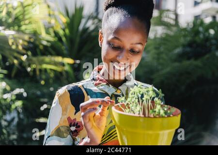 Porträt einer glücklichen jungen Frau, die im Blumentopf im Garten Sprossen beobachtet