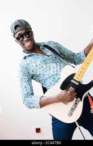 Portrait von glücklichen jungen Popmusiker Gitarre spielen vor weißem Hintergrund Stockfoto