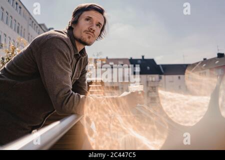 Mann, der sich auf das Balkongeländer lehnte und einen Drink hatte Stockfoto