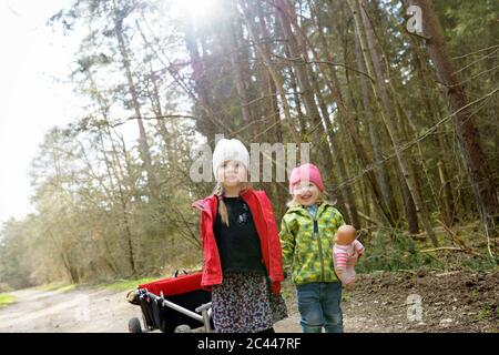 Zwei kleine Schwestern ziehen Trolley auf Waldweg Stockfoto