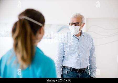 Der ältere Mann trifft sich mit seinem weiblichen Physiotherapeuten an der Rezeption und trägt Gesichtsmasken Stockfoto