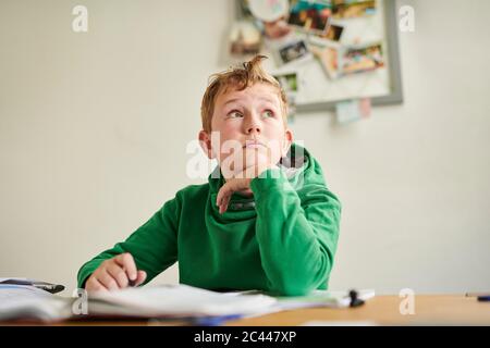 Nachdenklicher Junge schaut weg, während er zu Hause studiert Stockfoto