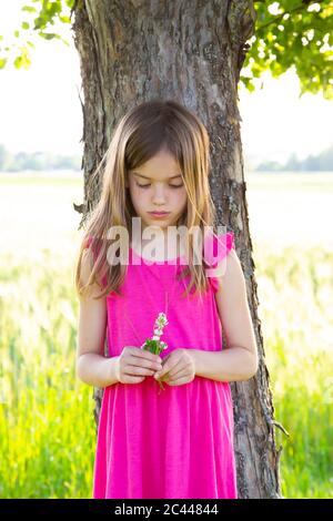 Portrait von kleinen Mädchen stehen unter apple tree mit Klee Blumen in den Händen Stockfoto