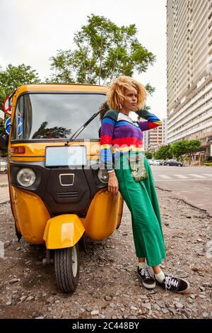 Volle Länge junge Frau mit afro Frisur lehnt auf Tuk-Tuk in der Stadt Stockfoto