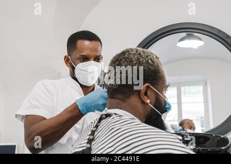 Friseur trägt chirurgische Maske und Handschuhe tun Haar des Kunden Stockfoto