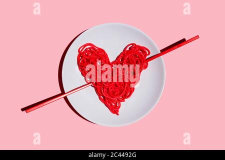 Studio Aufnahme von Teller mit roten herzförmigen Spaghetti vor rosa Hintergrund Stockfoto