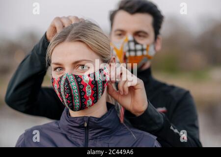 Portrait der jungen Frau, während Mann Anpassung Gesichtsmaske für sie im Park Stockfoto