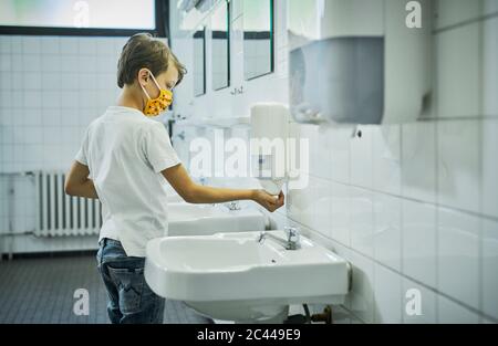 Junge trägt Maske auf der Schultoilette waschen seine Hände