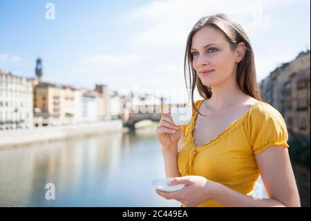 Porträt einer lächelnden Frau, die Espresso in der Nähe der Ponte Vecchio, Florenz, Italien genießt Stockfoto