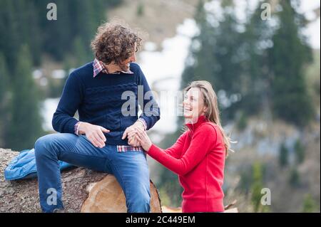 Glückliche Frau, die die Hand des Mannes auf dem Log sitzend hält Stockfoto