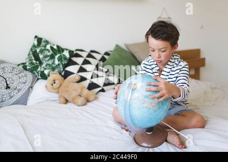 Porträt eines kleinen Jungen auf dem Bett mit seinem Globus sitzen Stockfoto