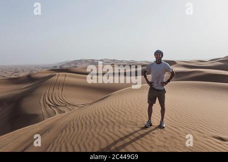 Glücklicher männlicher Tourist, der auf Sanddünen in der Wüste in Dubai, Vereinigte Arabische Emirate steht Stockfoto