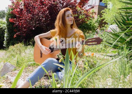 Lächelnde junge Frau spielt Gitarre in Natur Stockfoto