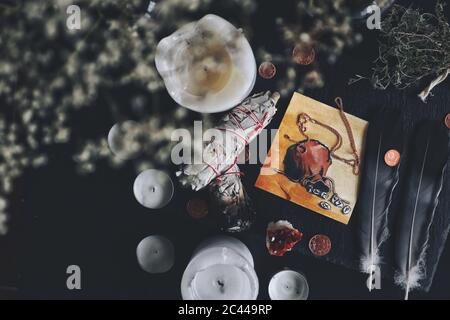 Flaches Lay Geld zieht Zauber auf Wiccan Hexenaltar. Illustration eines Beutels gefüllt mit Runen, dunkelgrauen schwarzen Federn, Kupfermünzen, Salbei-Sticks Stockfoto