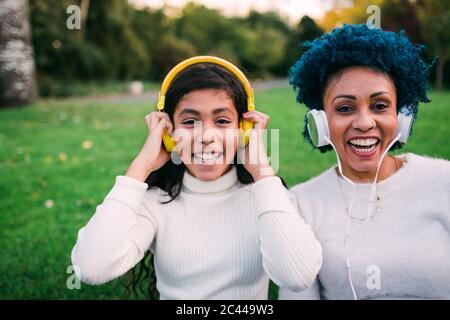 Glückliche Mutter und Tochter hören Musik über Kopfhörer im Park Stockfoto