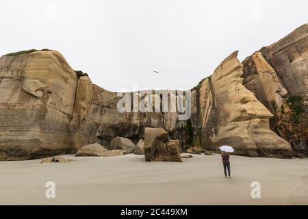 Neuseeland, Ozeanien, Südinsel, Otago, Dunedin, Frau mit Sonnenschirm in der Nähe von Klippen am Tunnel Beach Stockfoto