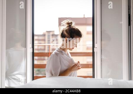 Seitenansicht der schönen jungen Frau, die zu Hause am Bett sitzt Stockfoto