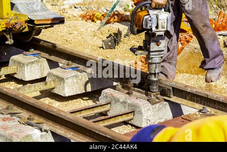 Bahnarbeiter, die die Gleisschiene verschrauben. Detailarbeiter mit leichter tragbarer Schlaffenbohrmaschine Stockfoto