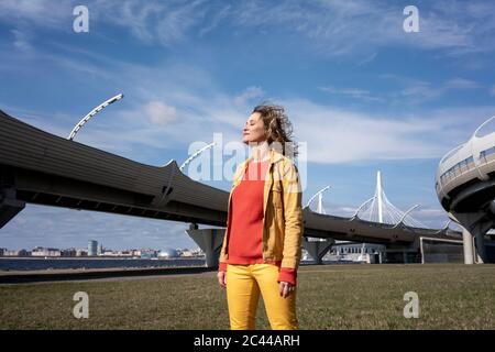 Lächelnde Frau mit windigen Haaren, die an einer Straßenbrücke stehen Stockfoto