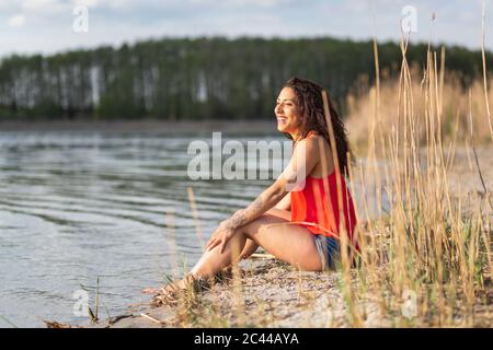 Porträt der glückliche junge Frau sitzt am Seeufer Stockfoto