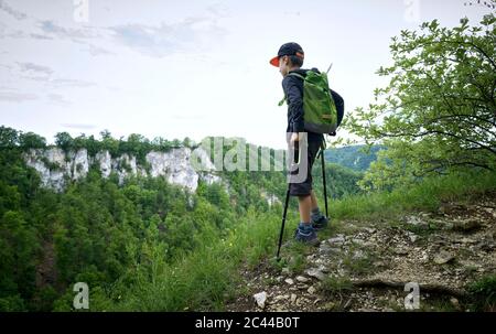 Junge steht mit Wanderstöcken am Rande des Plateaus und blickt auf die Landschaft der Schwäbischen Alb Stockfoto