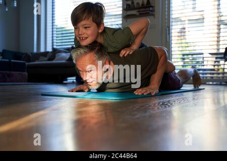 Junge beobachten seinen Vater tun ein Heim-Training, halten auf dem Rücken Stockfoto