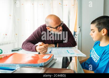 Vater erklärt Sohn sitzen am Schreibtisch während der Heimschooling Stockfoto