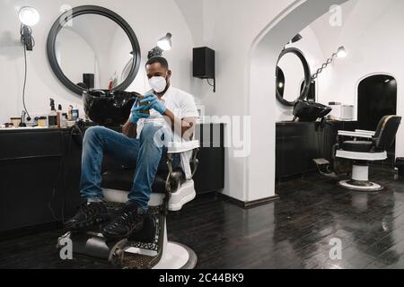 Friseur trägt chirurgische Maske und Handschuhe mit Smartphone Stockfoto