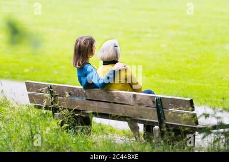 Ältere Frau und Erwachsene Tochter sitzen zusammen auf Parkbank Stockfoto
