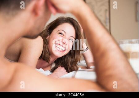 Fröhliche junge Frau, die den Mann ansieht, während sie zu Hause im Bett liegt