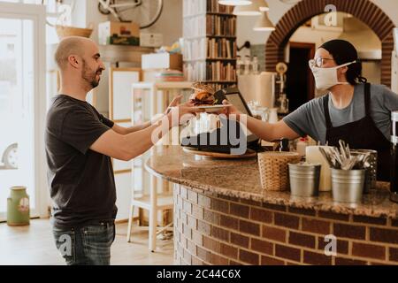 Kellnerin mit Schutzmaske serviert Essen in einem Café Stockfoto