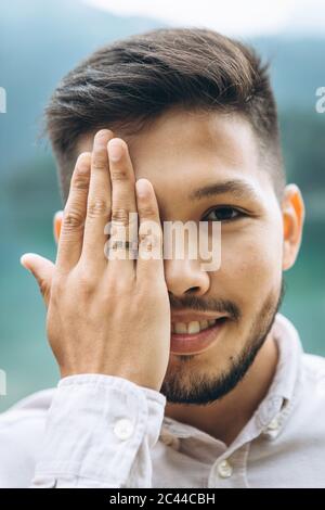 Junger Erwachsener schöner positiver Bräutigam schließt die Augen mit der Hand und zeigt einen Ehering an der Hand. Stockfoto