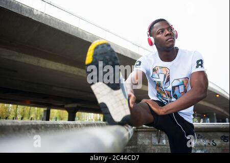 Junger Jogger, der sein Bein streckt und Musik in der Stadt hört Stockfoto